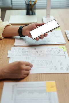 Woman checking financial documents while using smartphone at home. Monthly budgeting and expense tracking support bill payments, debt management and personal finance.