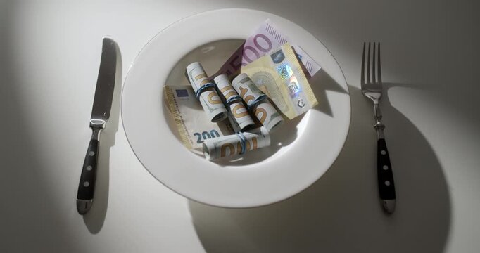 White plate filled with 100 US dollar banknotes arranged like a pasta on a white table with a fork and knife. Creative metaphor for extreme wealth, luxury, financial success, greed, money obsession