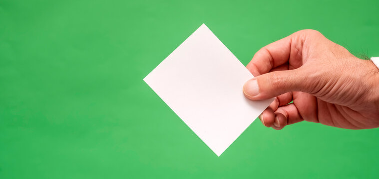 Male hand holding a blank white paper against a green backdrop. This versatile image is ideal for business presentations, marketing mockups, and compositing projects.