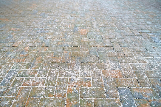 Closeup pavement, rock salt scattered across paving slabs to reduce ice buildup and minimize slipping risks for pedestrians during frosty winter conditions in an urban environment, selective focus