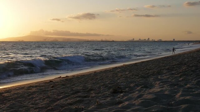 View from Sunset Beach in Huntington Beach, California. Long Beach industry and oil rigs, waves and children playing in the Pacific Ocean surf.