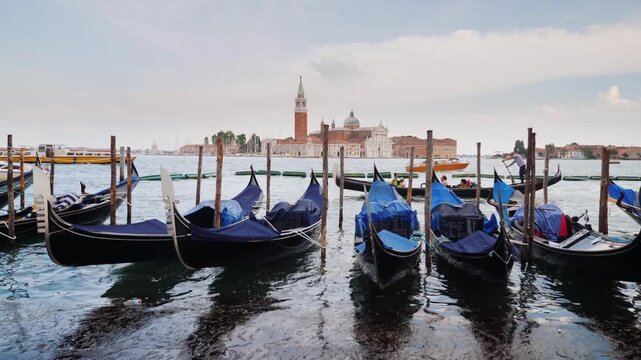 Cinematic view of traditional gondolas moored in Venice with San Giorgio Maggiore church in distance.