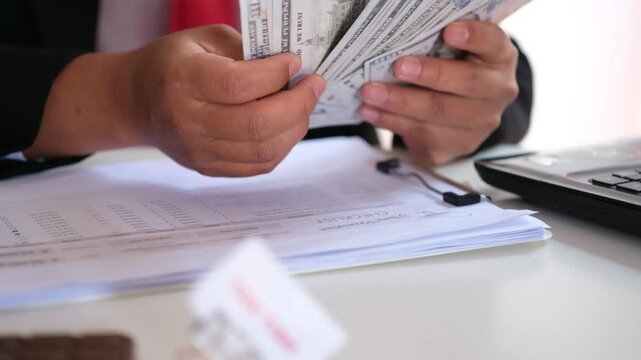 TAX TIME written on a clipped paper on a desk; tax season concept. Background featuring an employee counting money. Concept of tax payment planning and calculation; money and finance concept; tax evas