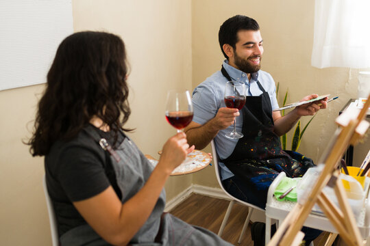 Happy couple enjoying a creative paint and sip event, drinking red wine and painting during an art class