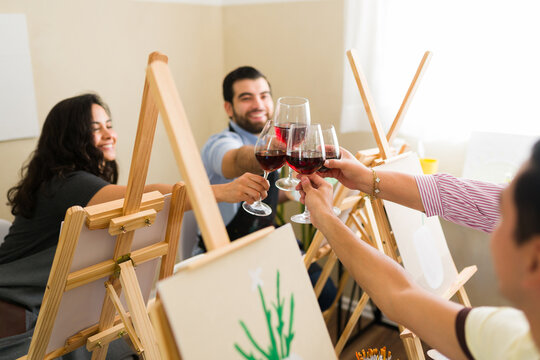 Group of friends enjoying an adult painting class and toasting with red wine glasses at a fun art workshop