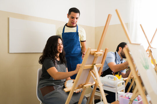 Students learning painting in an art workshop, instructor guiding woman creating artwork on canvas