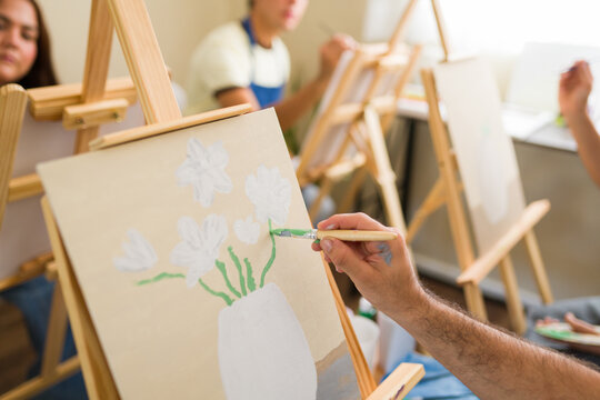 Adult art class participant painting flowers on a canvas during an engaging creative workshop or hobby session