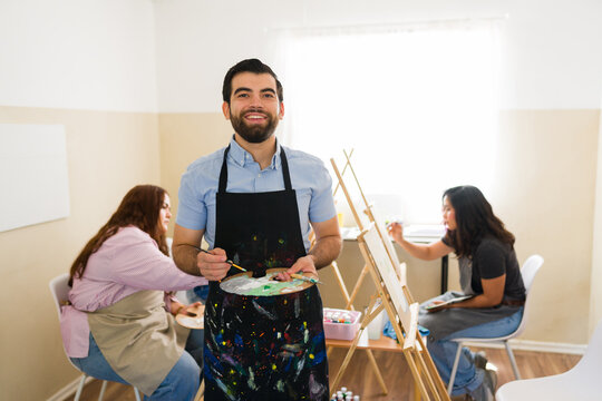 Happy man holding palette and paintbrush during an adult art class, enjoying a creative hobby and learning new skills