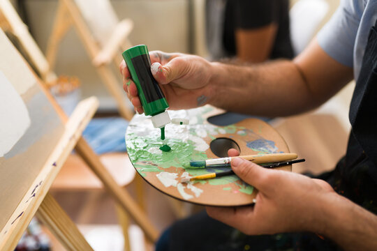 Artist hands squeezing green paint onto a wooden palette during an adult art class, creating color for a new painting