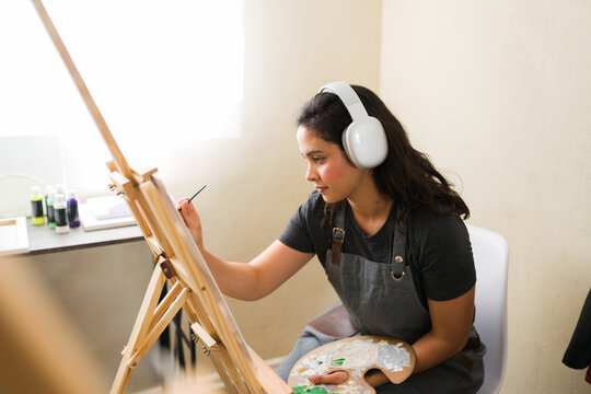 Profile view of a woman painting on a canvas during an adult art class, focusing on her artwork and enjoying a creative hobby