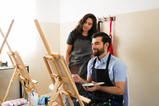 Adults learning to paint in art class, instructor guiding student during creative workshop