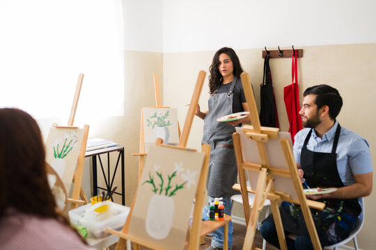 Adult art class attendees learning painting techniques from a female teacher during a creative workshop session