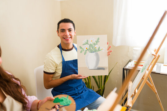 Happy man holding painting showing flowers in a vase, proudly displaying his artwork in an adult art class studio