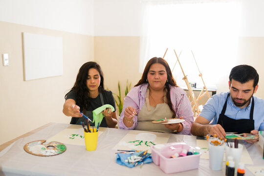 Friends learning painting techniques during an art class, enjoying a creative workshop and developing artistic skills