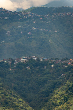Densely forested mountain slopes dotted with hillside homes and communities, with low clouds and mist creating an atmospheric tropical highland landscape.
