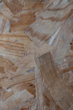 Close-up of rough engineered wood made from compressed wood flakes, showing overlapping grain, chips, fibers, and natural brown tones as an abstract construction texture.