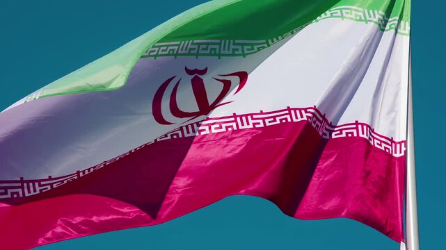 Iranian Flag Wiggles the Wind. The Big State Flag is illuminated by the sun and flutters epically in the wind against the blue sky