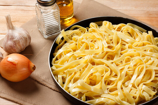 Fettuccine pasta prepared in a dark skillet on a rustic surface, surrounded by fresh Italian seasoning ingredients.