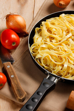 Fettuccine ready to serve in a black skillet on rustic wood, accompanied by staple Mediterranean ingredients.