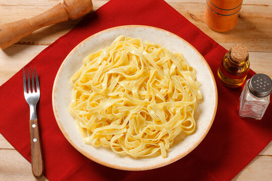 Fettuccine pasta prepared and served on a handcrafted plate on a wooden table, with a red napkin.