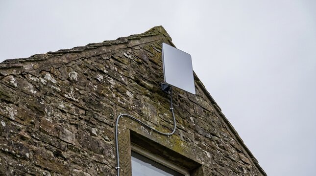 A Plain Rectangular Satellite Internet Dish Mounted On A Stone House Gable Showing Rural Connectivity