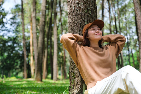 Portrait image of a woman with closed eyes sitting and putting hands behind her neck for relaxing in the park