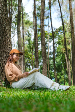 Vertical portrait image of a woman reading a book while sitting in the park