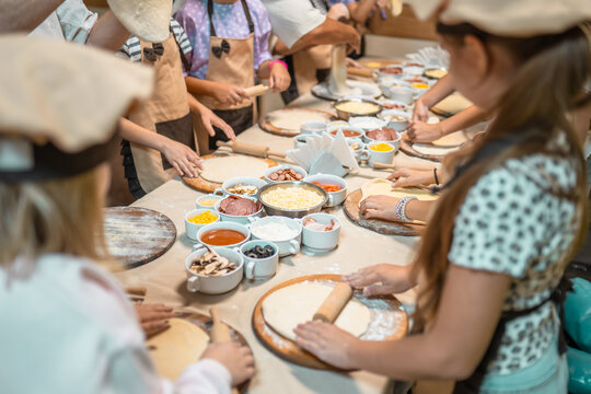 Group of kids in aprons and chef hats preparing homemade pizza during culinary workshop