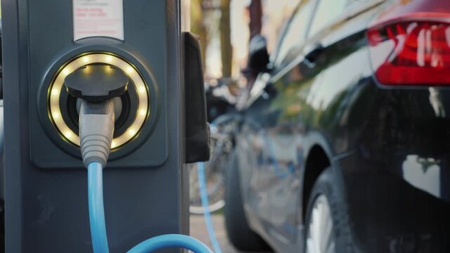 Electric car charging station with blue cable plugged into power socket in urban street environment.