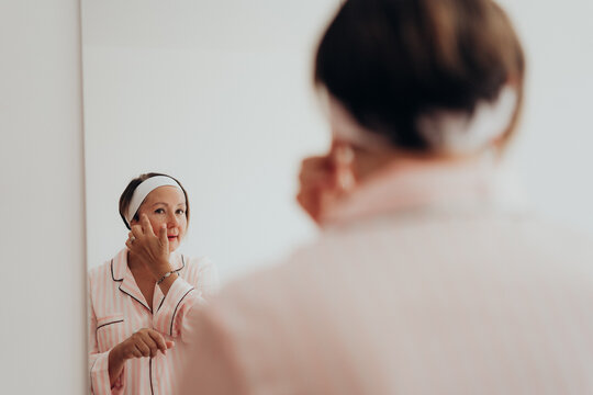 Mature woman with skincare tube reflected in mirror during home beauty routine for neck care decollete care anti aging skin firming wrinkle care and collagen support