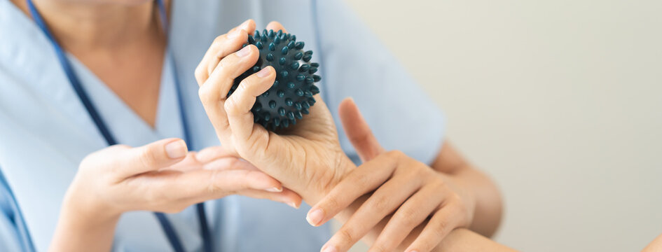 Close up of a physical therapist helping a patient exercise with a spiky massage ball for hand rehabilitation, occupational therapy and stroke recovery medical concept.