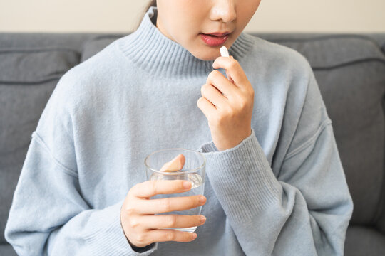 Sick, asian young woman, girl hand holding pill, painkiller medicine from stomach pain, headache, pain for treatment, take drug or vitamin and glass of water at home, pharmacy and health care concept.
