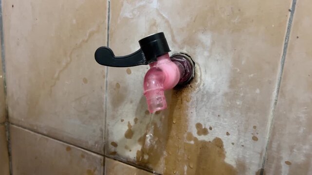 Worn pink faucet with water flowing steadily onto a mineral-stained tiled wall.