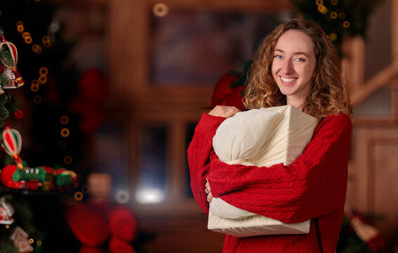 smiling young woman holding a wrapped Christmas gift in a cozy and festive holiday living room
