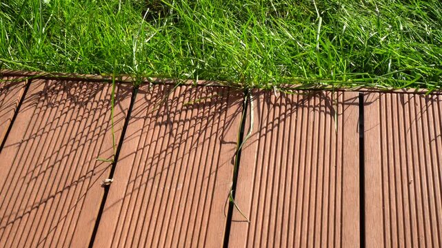 Wooden deck boards with ribbed texture bordering a lush green lawn in a sunny garden landscape