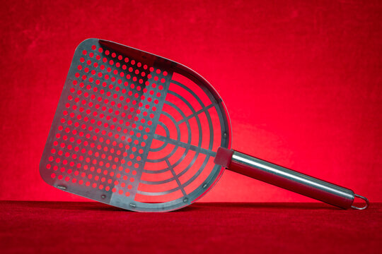 Metal perforated cat litter scoop on red background