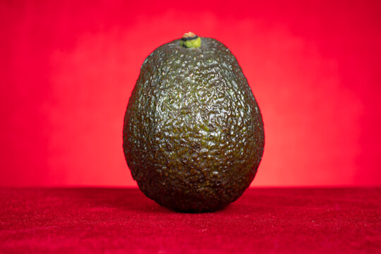 Whole ripe avocado on red fabric surface