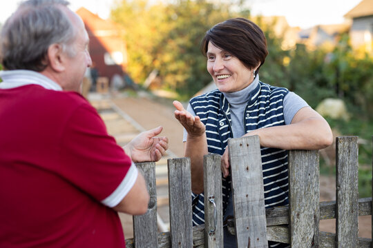 Two gardeners friendly talking outdoors next to wooden fence of country estate on day