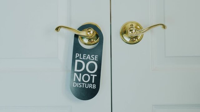 Woman hand placing do not disturb sign on hotel room door handle, privacy request.