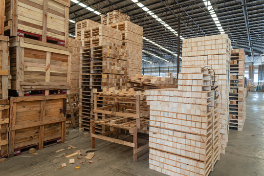 Wooden pallets in a warehouse stack stand beside wooden crates and red pallet bases within an empty storage area.