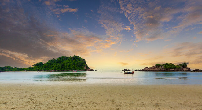 Tropical Beach Sunset Landscape with Small Island and Fishing Boat,A scenic landscape photograph of a tranquil tropical sandy beach at sunset, featuring calm sea water, small green islands, and a trad