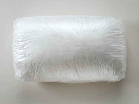 A white, plump pillow in clear plastic packaging is centered against a transparent background The wrapping shows subtle creases and reflects light It appears to be new or recently pac - AI-Generated