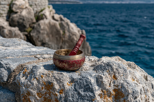 Small ornate meditation singing bowl resting on a large coastal rock near