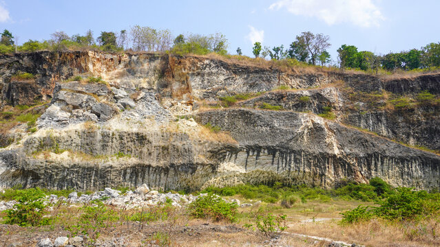 Former limestone quarry site in Sukolilo, Pati, Central Java, Indonesia. Rugged cliff face of open-pit mine showing excavated white stone layers for cement and construction material production.