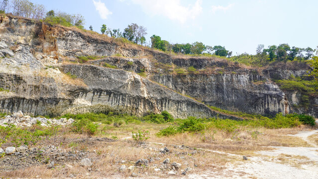 Former limestone quarry site in Sukolilo, Pati, Central Java, Indonesia. Rugged cliff face of open-pit mine showing excavated white stone layers for cement and construction material production.