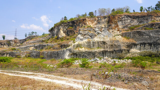 Former limestone quarry site in Sukolilo, Pati, Central Java, Indonesia. Rugged cliff face of open-pit mine showing excavated white stone layers for cement and construction material production.