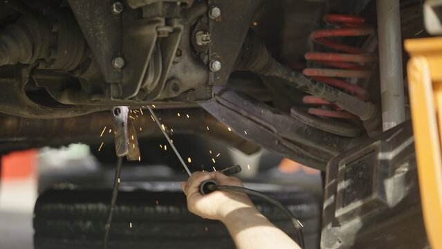 Car mechanic welding under the car fixing broken parts