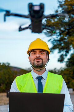 Man in safety gear operating drone with laptop outdoors in clear sky