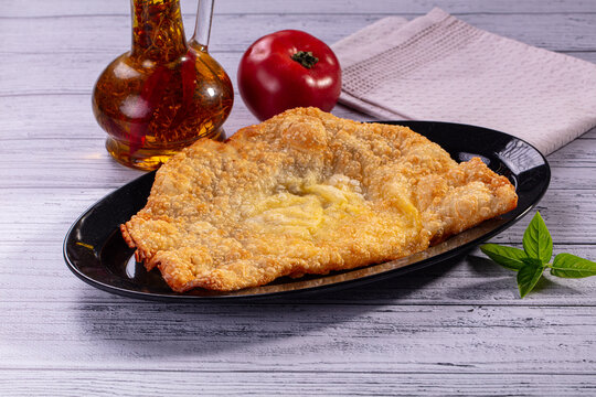 Golden fried cheburek on black plate with tomato and oil bottle