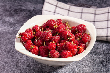 Fresh red raspberries in white ceramic bowl on dark textured surface with checkered cloth background © Andrei Starostin